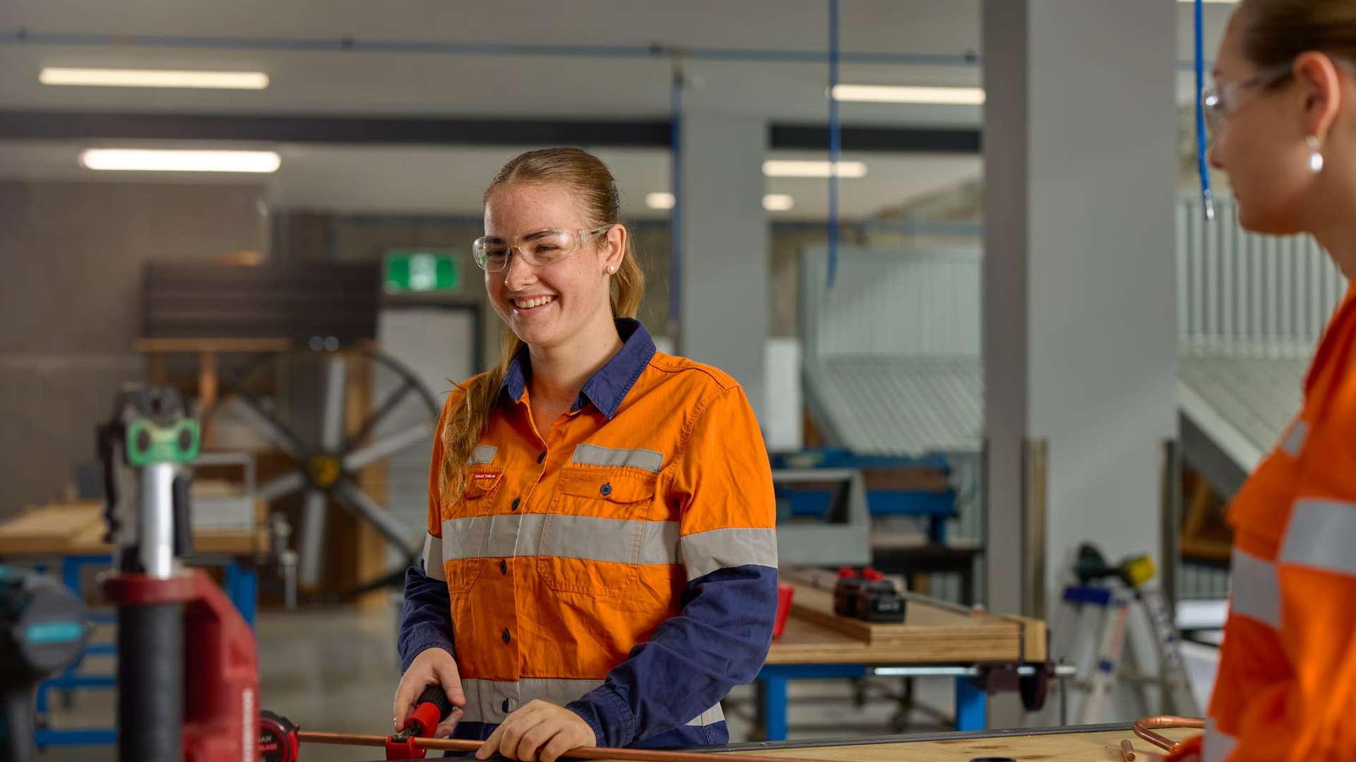 Student wearing a high vis long sleeve shirt and safety glasses cutting a piece of metal pipe in the TAFE Excellence workshop