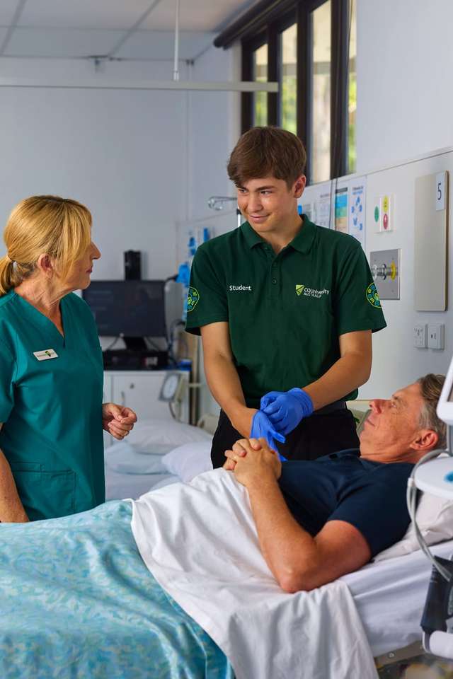 Nursing student standing with a lecturer at the bed of a patient in the practice nursing lab