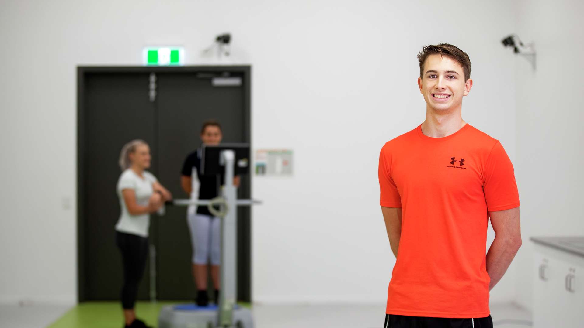 Exercise & Sports Science Student smiling in the foreground as people train in the background.