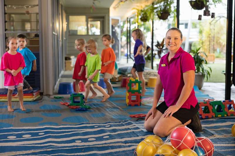 Child care worker sitting on floor surrounded by children