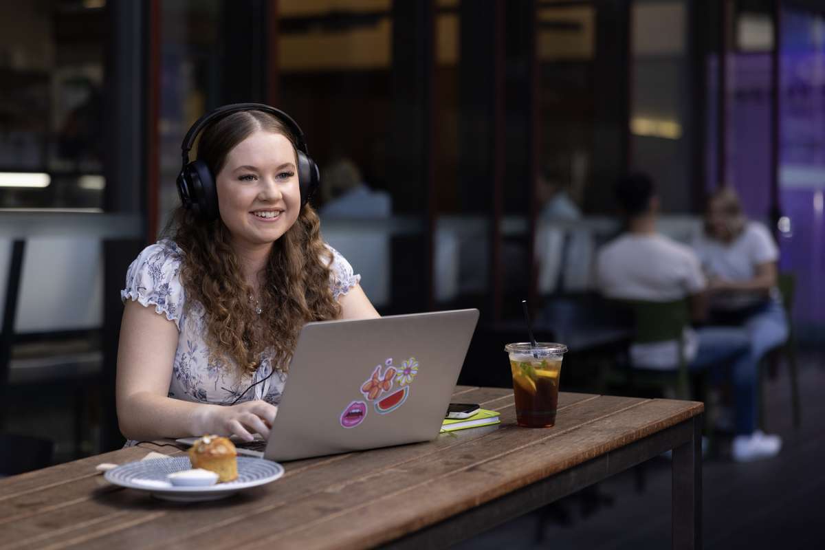 High School student sitting outside a cafe with a laptop and headphones studying