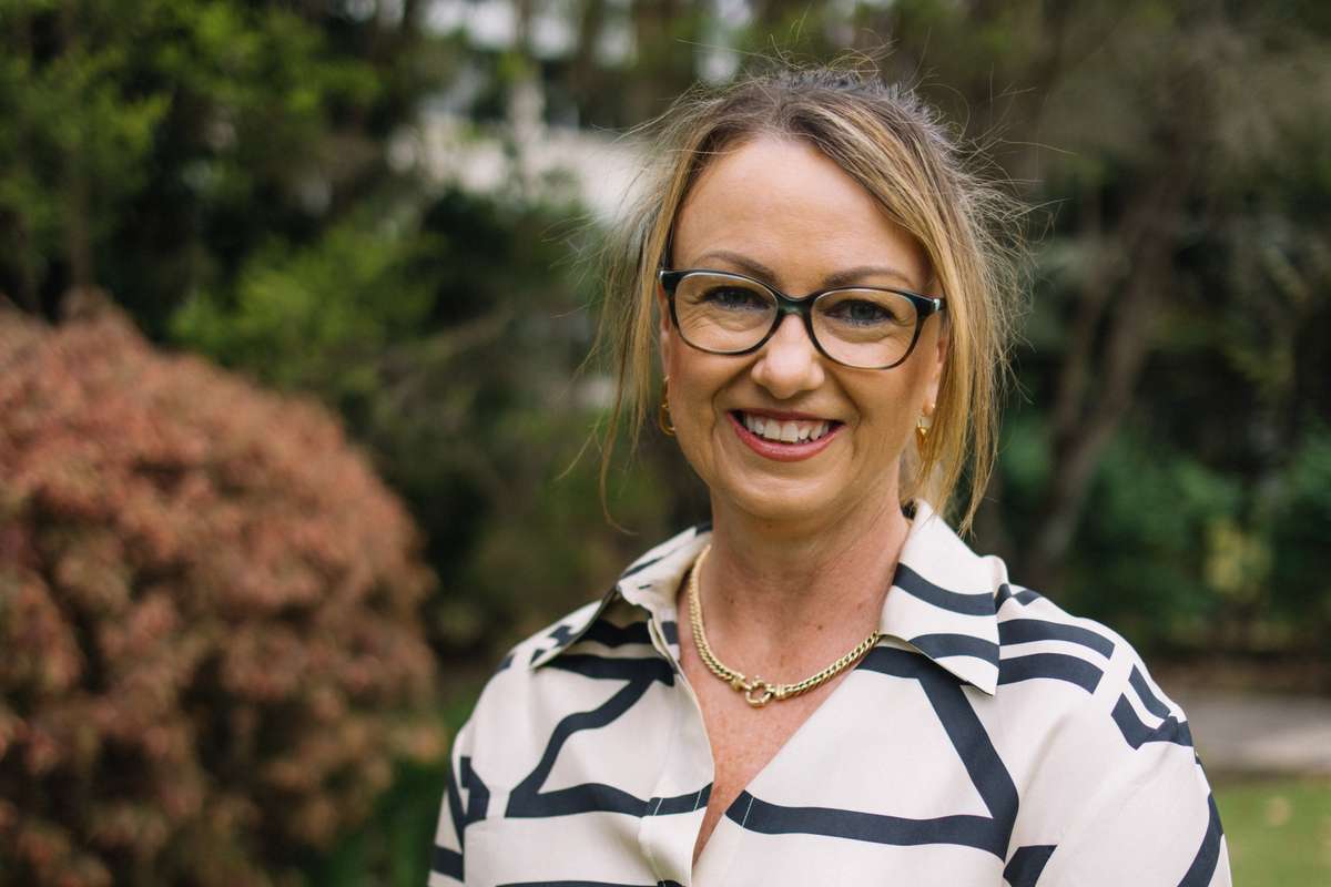 Narelle Pearse standing in front of greenery smiling at the camera with hands placed in front of her