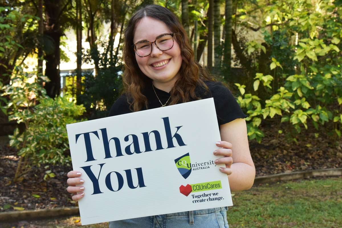 Chloe Coombe standing in front of a garden smiling and holding a sign that says thank you