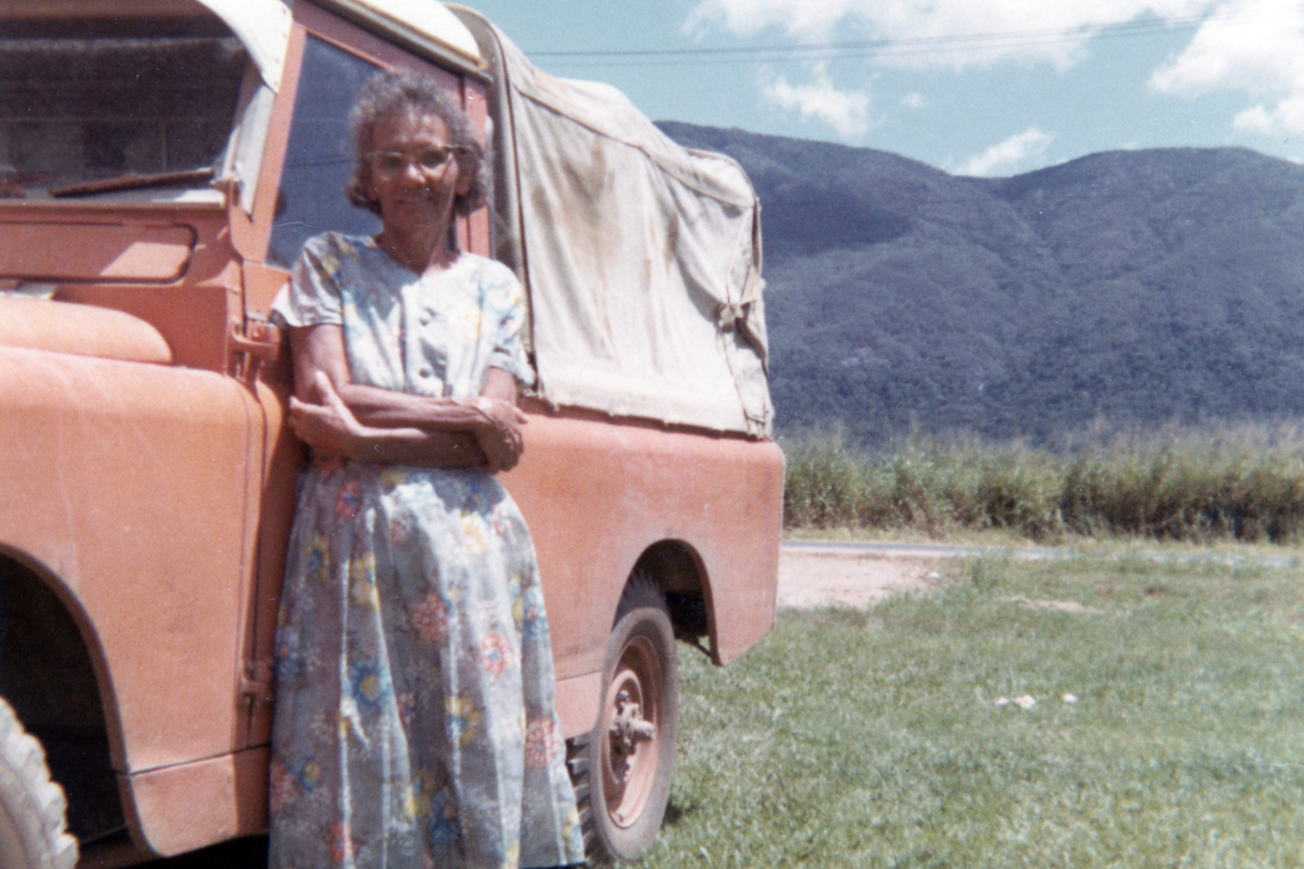 Chloe Grant stands with arms folded beside a red utility vehicle parked on grass.