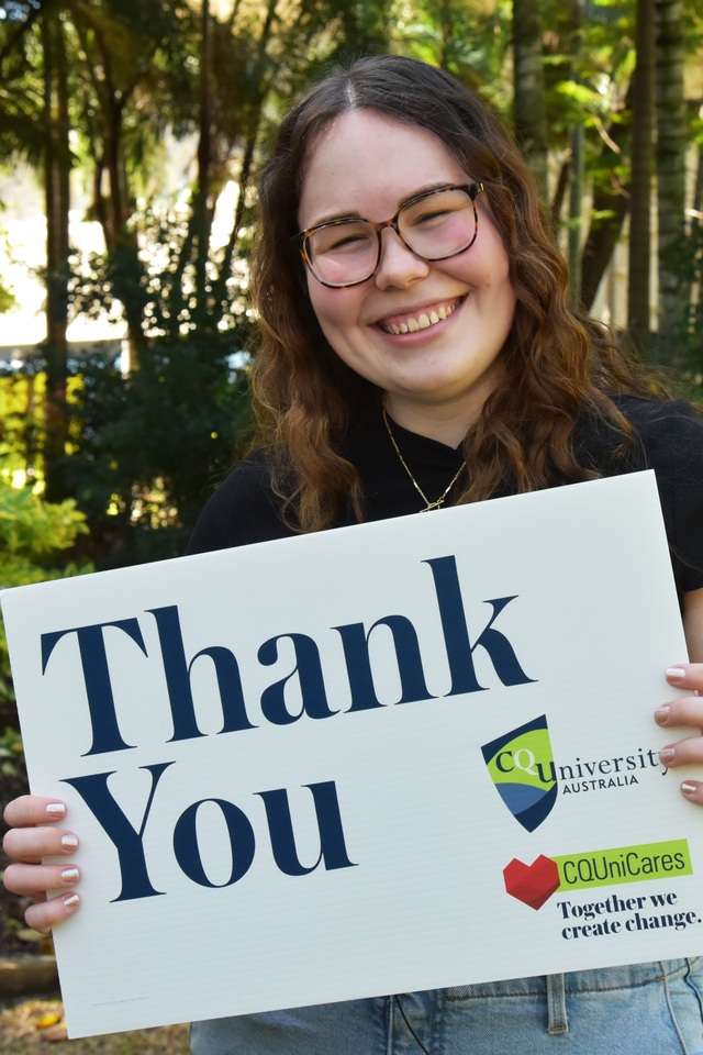 Chloe Coombe standing in front of a garden smiling and holding a sign that says thank you