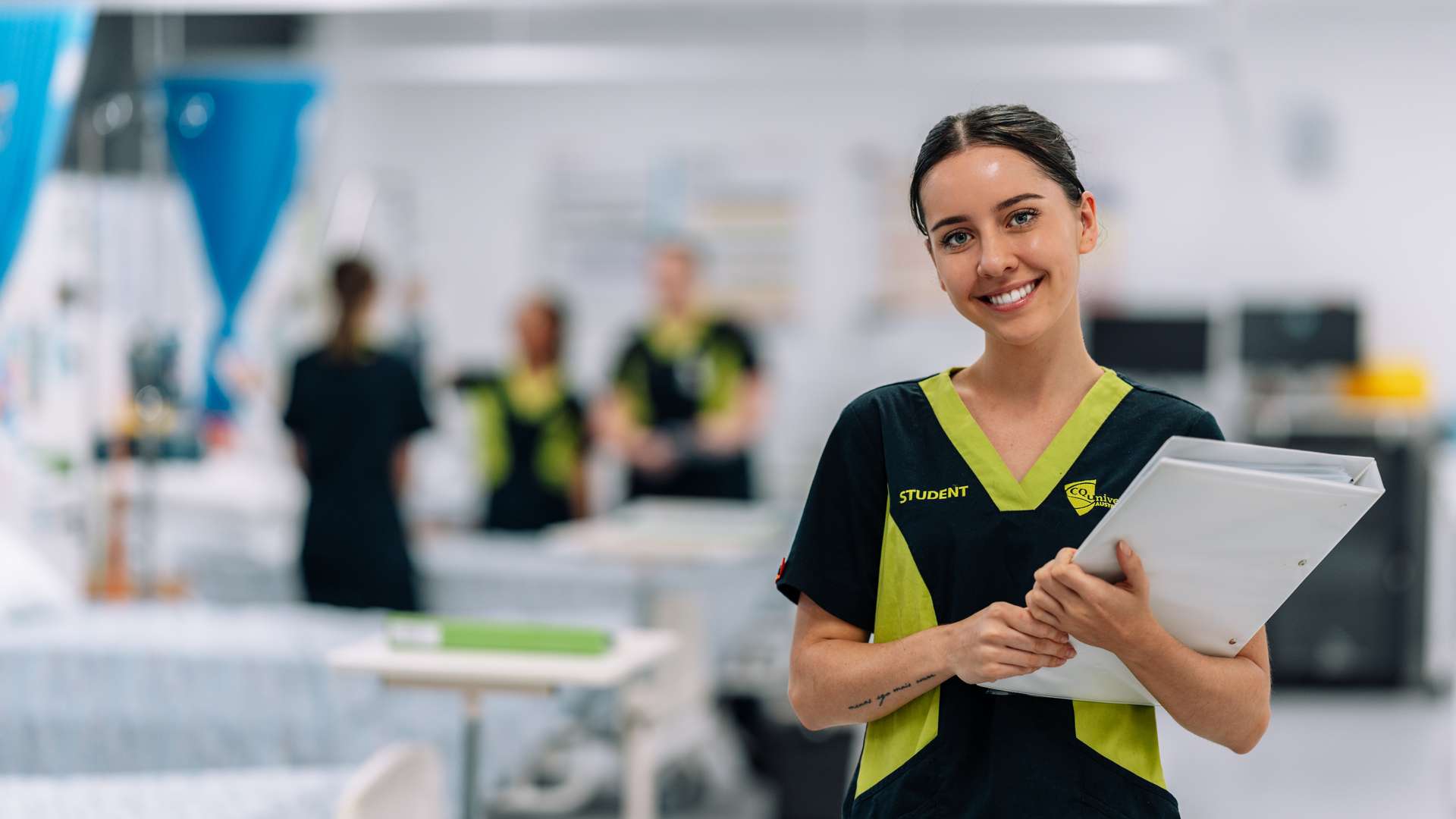 Nursing student with binder and peers in background in practical setting