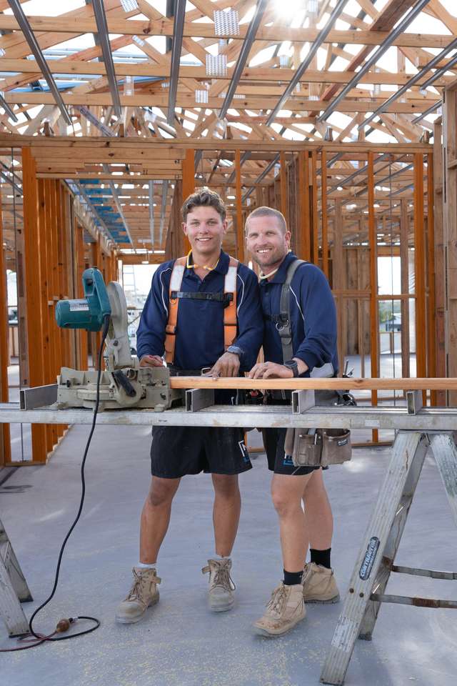 A CQU TAFE Construction student learns the tools with his builder overseeing his work on a job. They are standing in a house under construction.