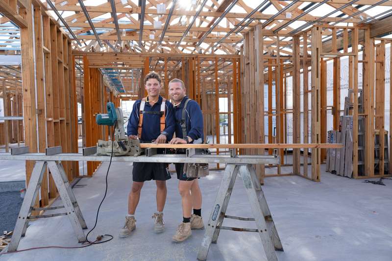 A CQU TAFE Construction student learns the tools with his builder overseeing his work on a job. They are standing in a house under construction.