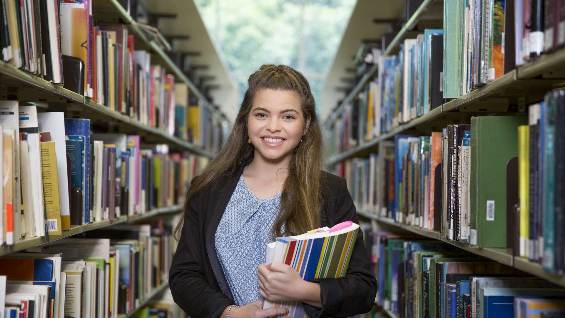 A smiling CQU student standing in library holding books
