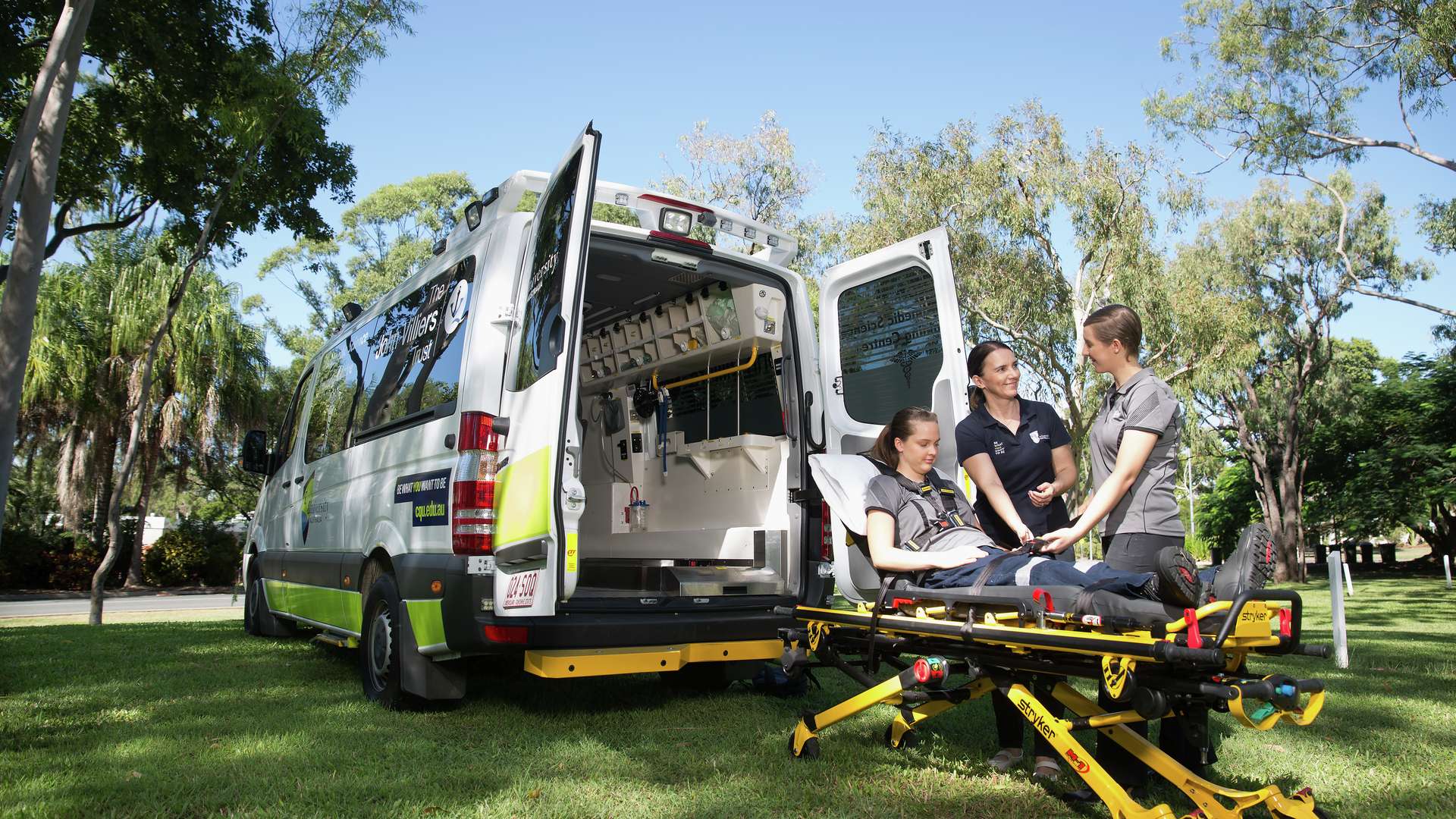 Two paramedic students practice using a stretcher while being guided by a lecturer