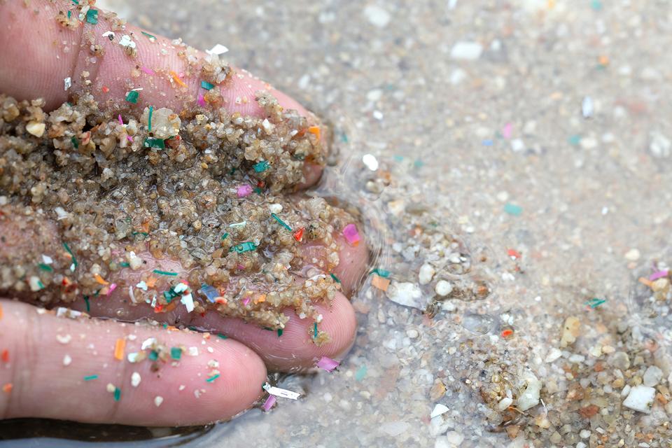 Close up of hand showing a large amount of micro plastic in the sand at the ocean edge
