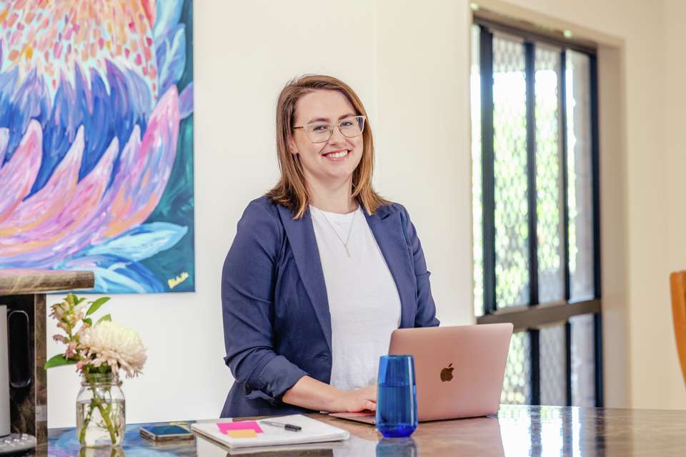 Student smiling and sitting at laptop with notepad with bright painting in background.