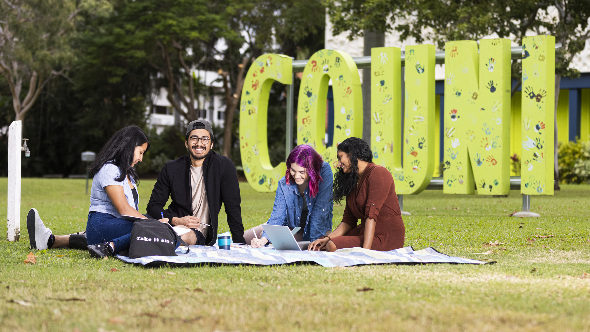 Four students sitting on a blanket on the CQU campus