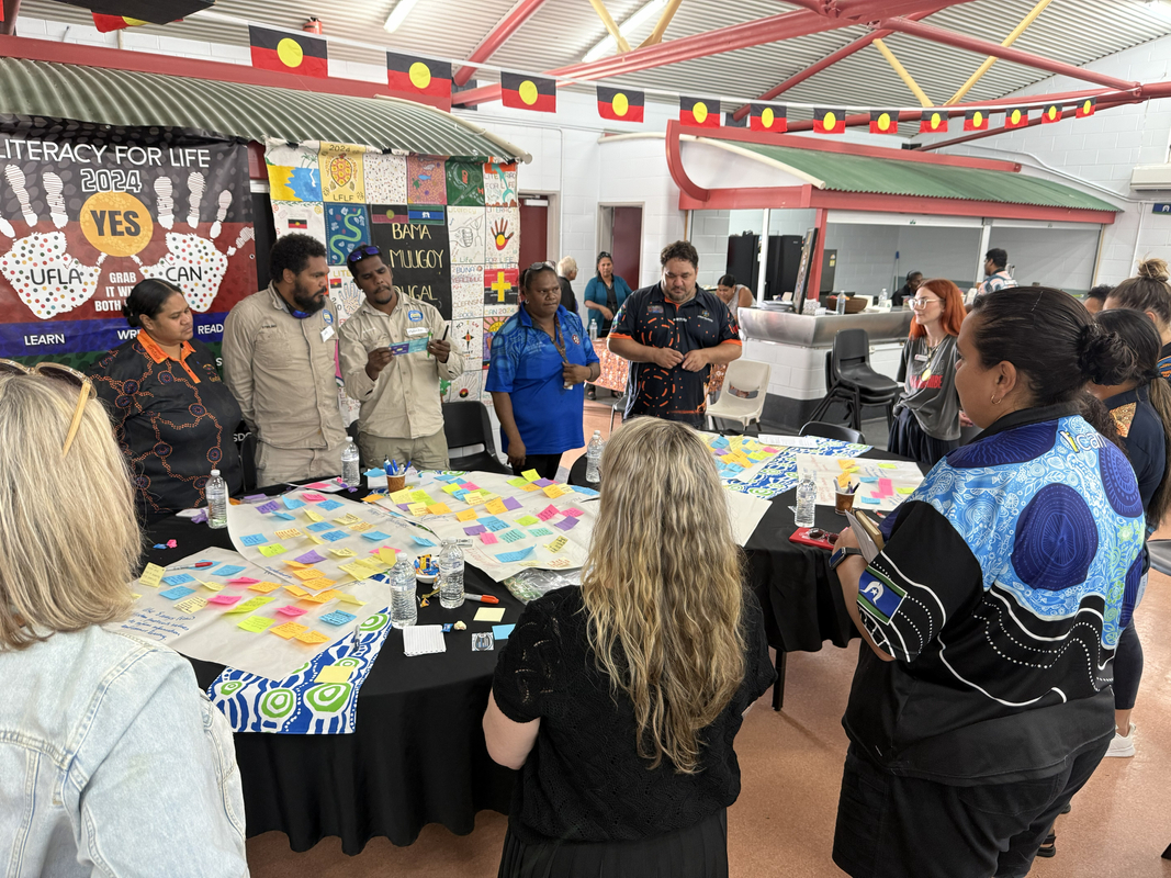 People gathered around a table covered with colorful sticky notes and papers during a community forum.