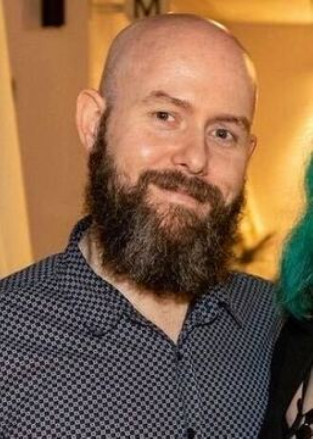 Glenn Wauchop with beard smiling, wearing blue, collared shirt