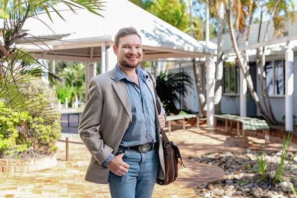 Daniel Hicks at a cqu campus standing and smiling at the camera with a sachel over his shoulder