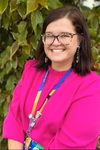 Danielle Stranieri wearing colourful clothing smiling for the camera in front of green shrubbery