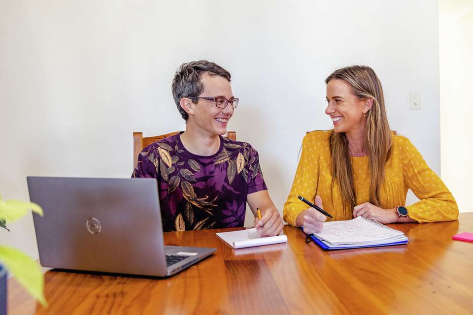 Two happy students taking notes while studying online from home with a laptop