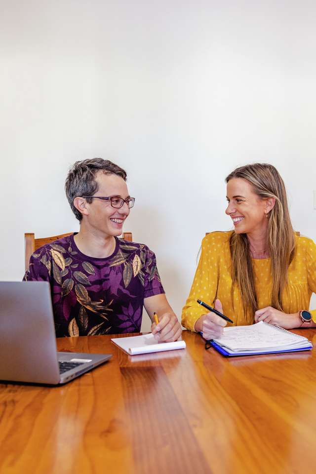 Two happy students taking notes while studying online from home with a laptop