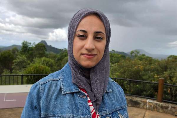 Farah Shakarchi wearing a headscarf and a denim jacket stands at an outdoor lookout area