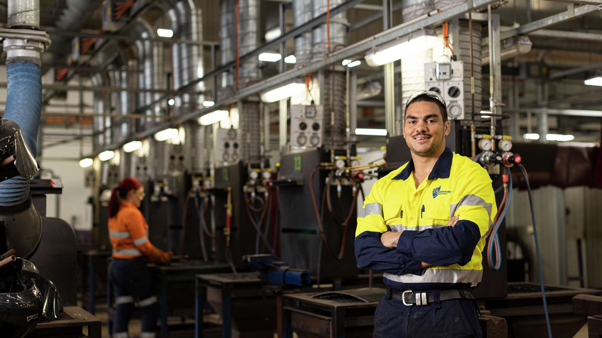First Nations student in PPE standing in a trades workshop smiling at the camera