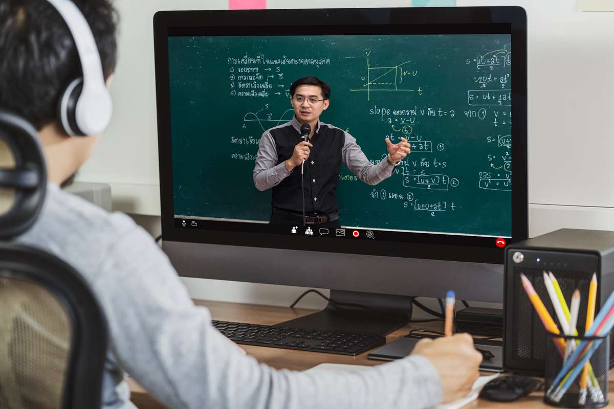 Male teacher teaching equations via video with a student on a desktop computer with headphones