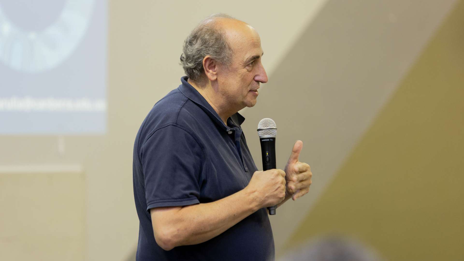 A man holder a microphone talking an at event.