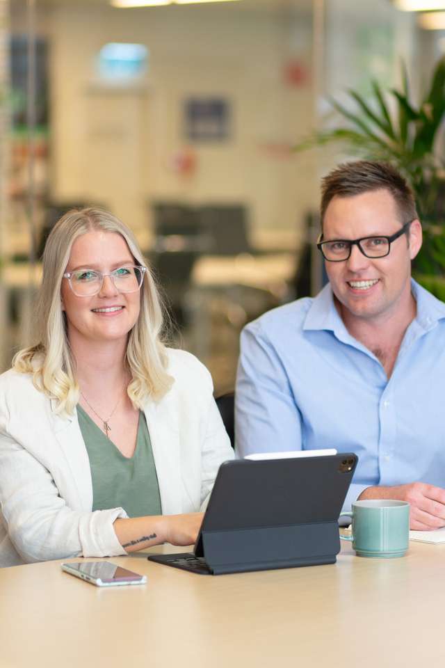 A male and female student smiling with a laptop open