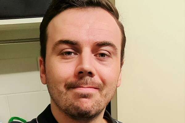 Scottish student, Hamish Summers wearing the CQU Physiotherapy uniform smiling in front of a white wall