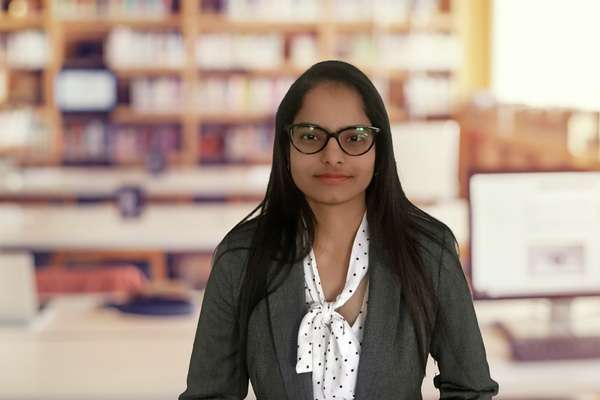 Harwinder Dhaliwal Kaur standing in a library smiling at the camera