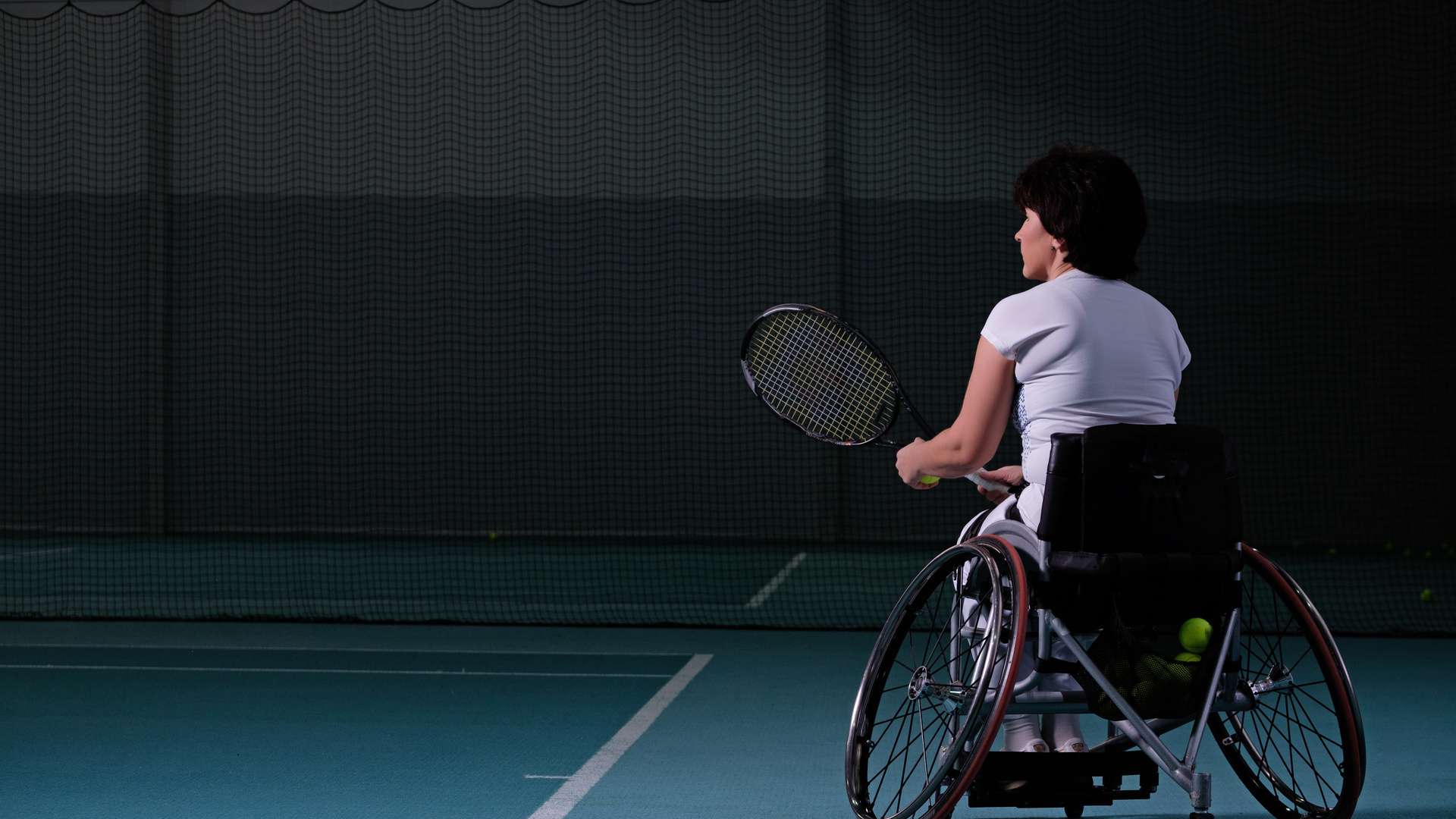 Disabled mature woman on wheelchair playing tennis on tennis court
