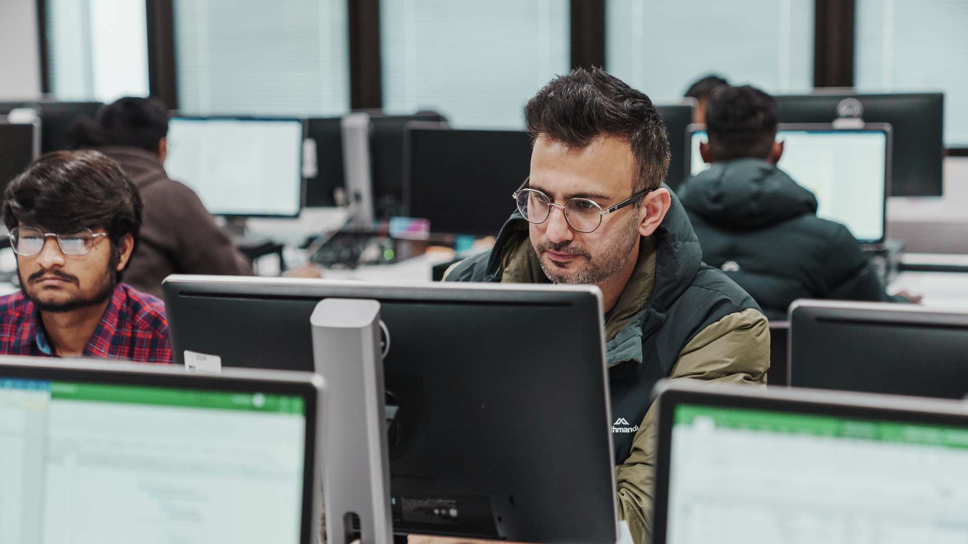 A Melbourne CQU student with glasses in tutorial room looking at computer screen.