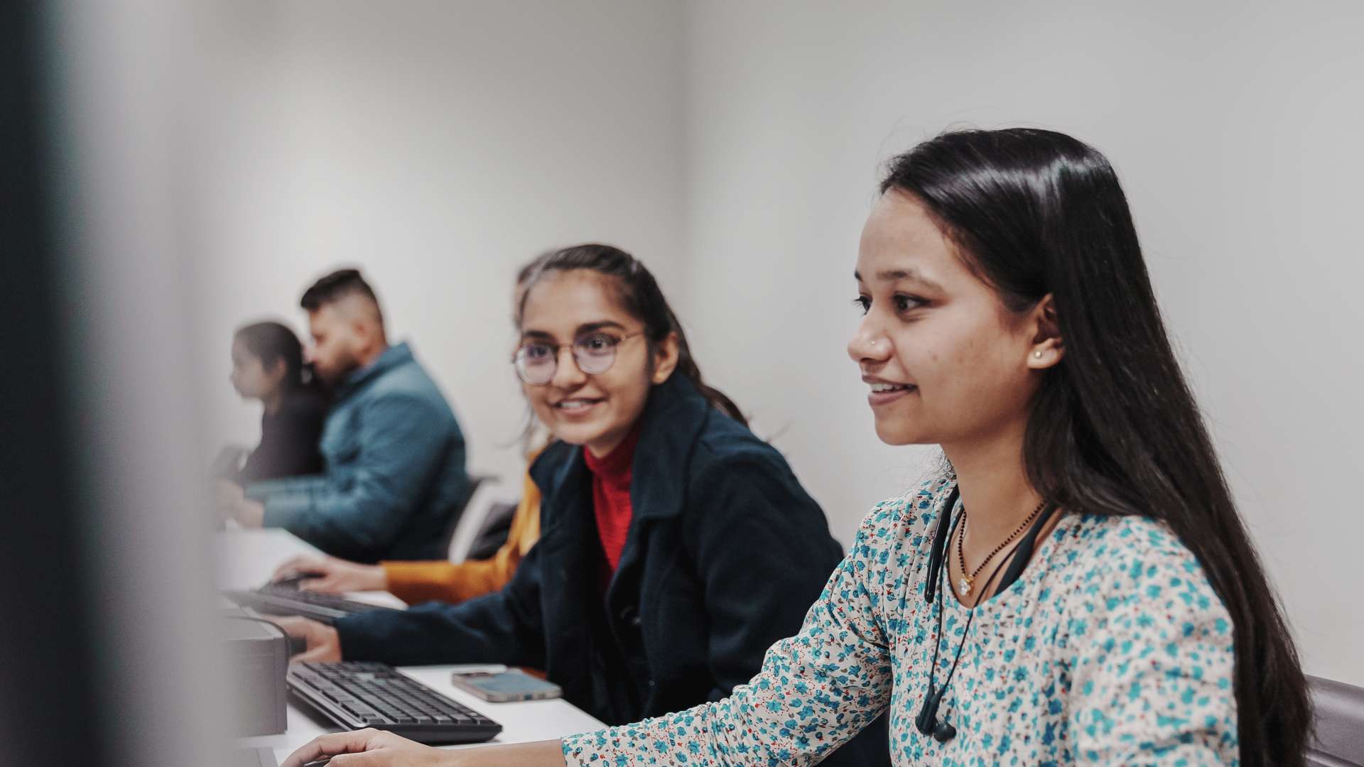 Two Melbourne CQU students in tutorial room talking with each other whilst on computer.