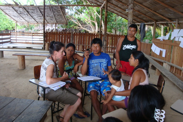 Small group gathered under a thatched roof structure, seated at desks with notebooks and papers