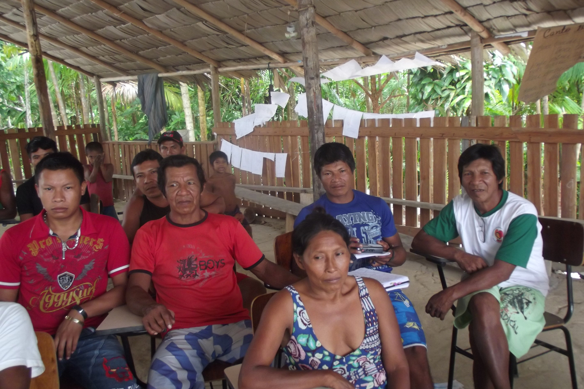 Several people seated at desks under a thatched roof structure