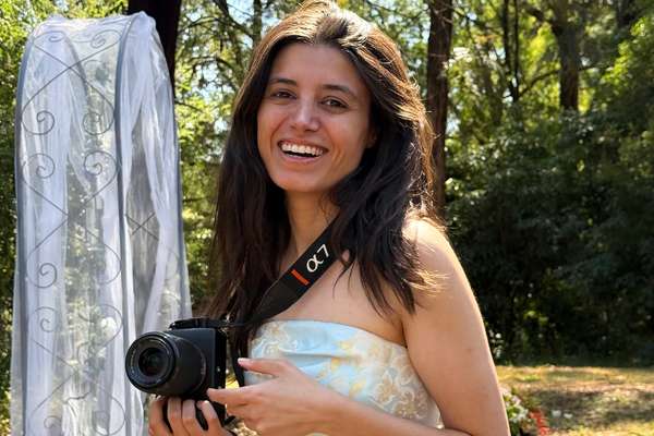 Irem Aydin holding a camera with a shoulder strap stands outdoors