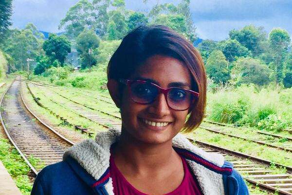 Ishani Senanayake, a student from Sri Lanka, smiling in front of train tacks and trees