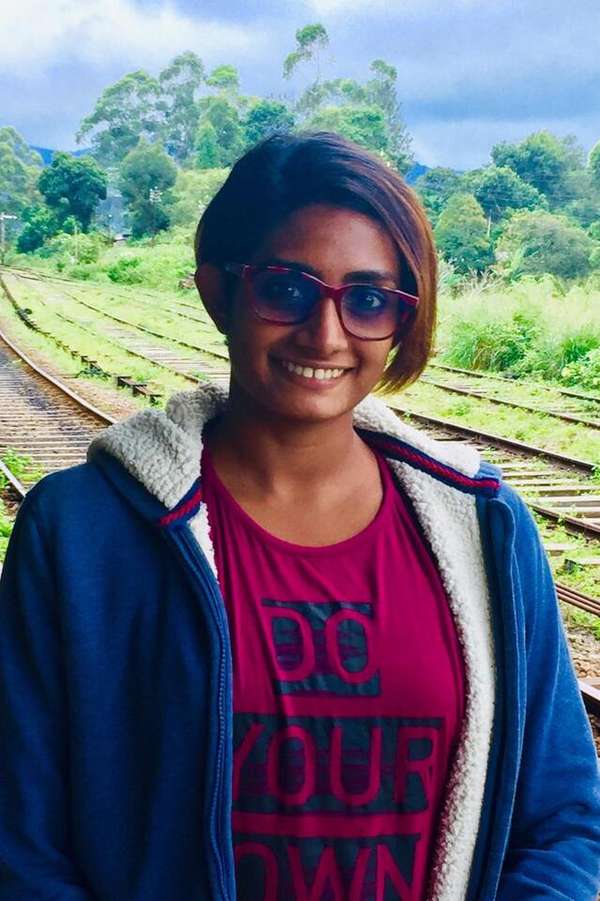 Ishani Senanayake, a student from Sri Lanka, smiling in front of train tacks and trees