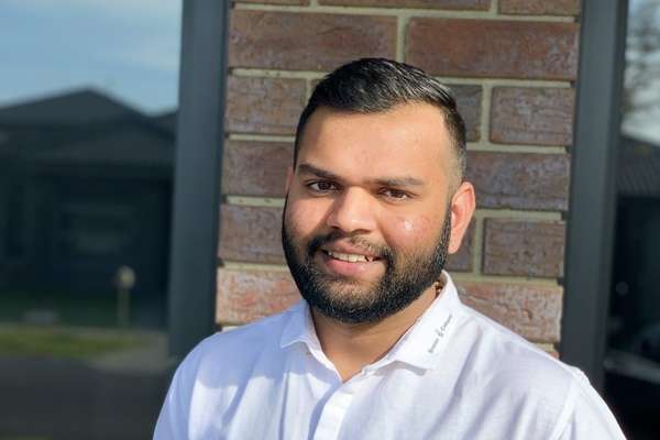 Masters student, Jayesh Dhirubhai Satani, from India, smiling in front of a brick wall and windows