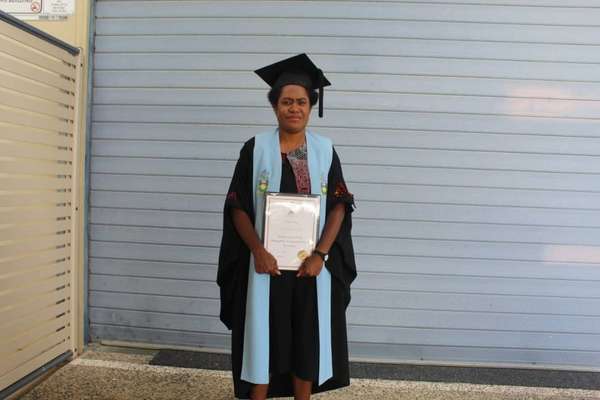 Jerusa Tilau at graduation in regalia holding the graduation certificate