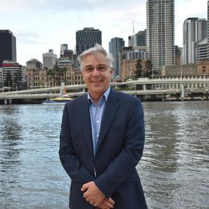 Jonathan Love standing infront of the Brisbane River in a suit smiling at the camera