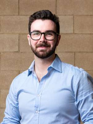 Josh Walker smiling wearing glasses and blue button up shirt