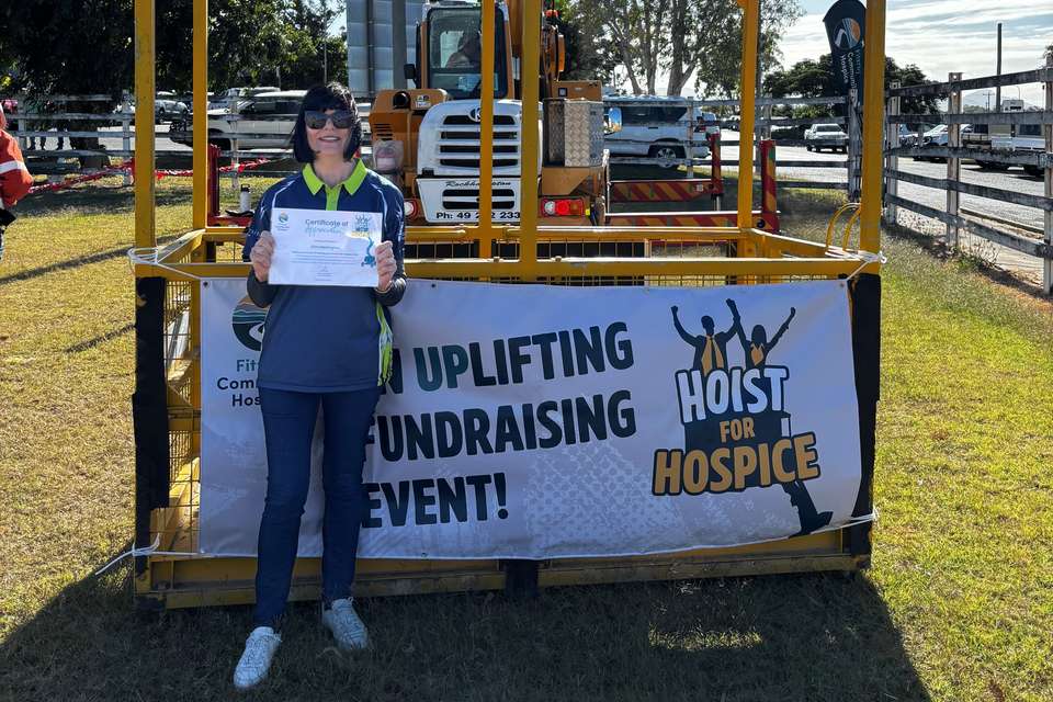 Kim Harrington stands next to a crane box, holding a certificate.