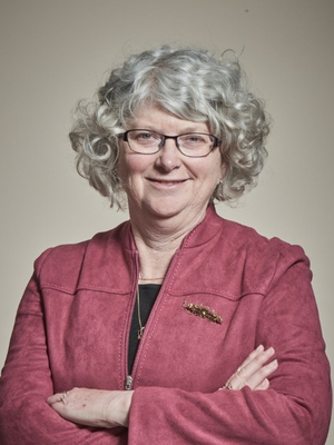 Kris Peach wears glasses stands against a plain background with arms crossed.