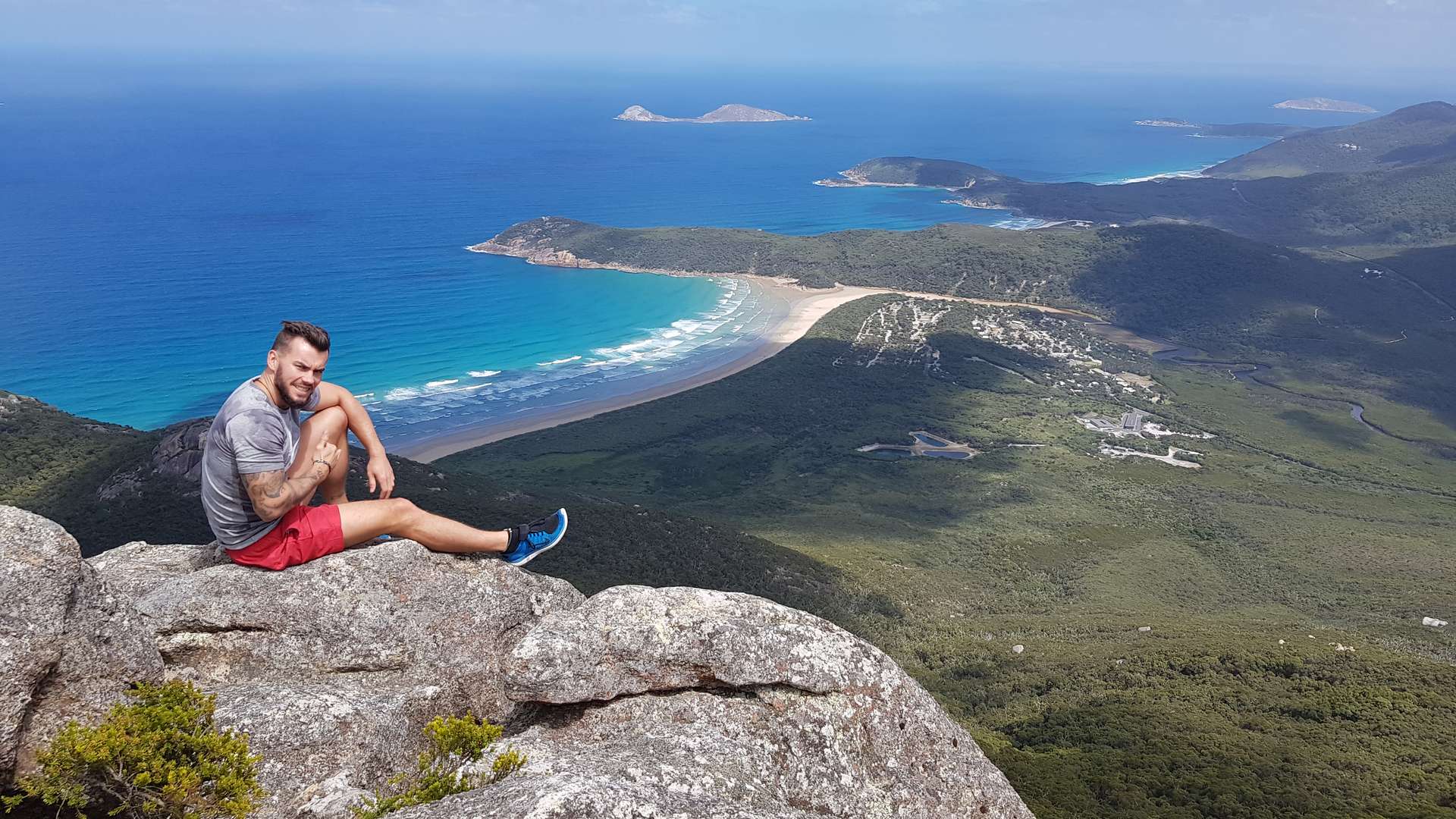 Global student seated on an elevated mountain rock with a blue beach in the background.