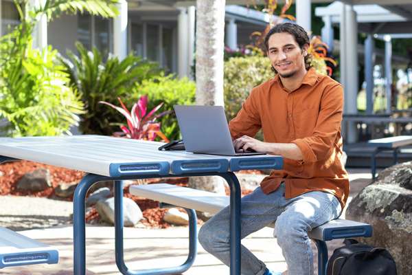 A First Nations student studying outside using a laptop