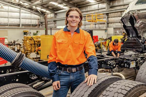 TAFE student Levi Bellette in high-vis work-wear standing beside a heavy vehicle in a workshop.