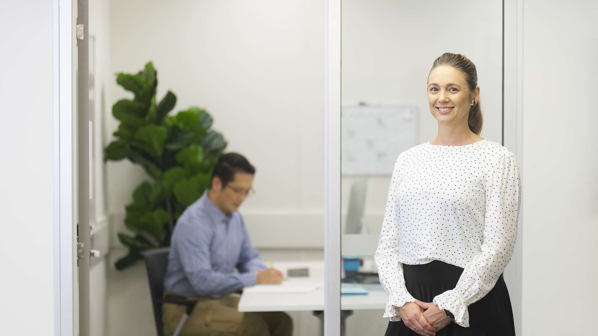 CQU student standing outside office smiling, with another student sitting inside office reading