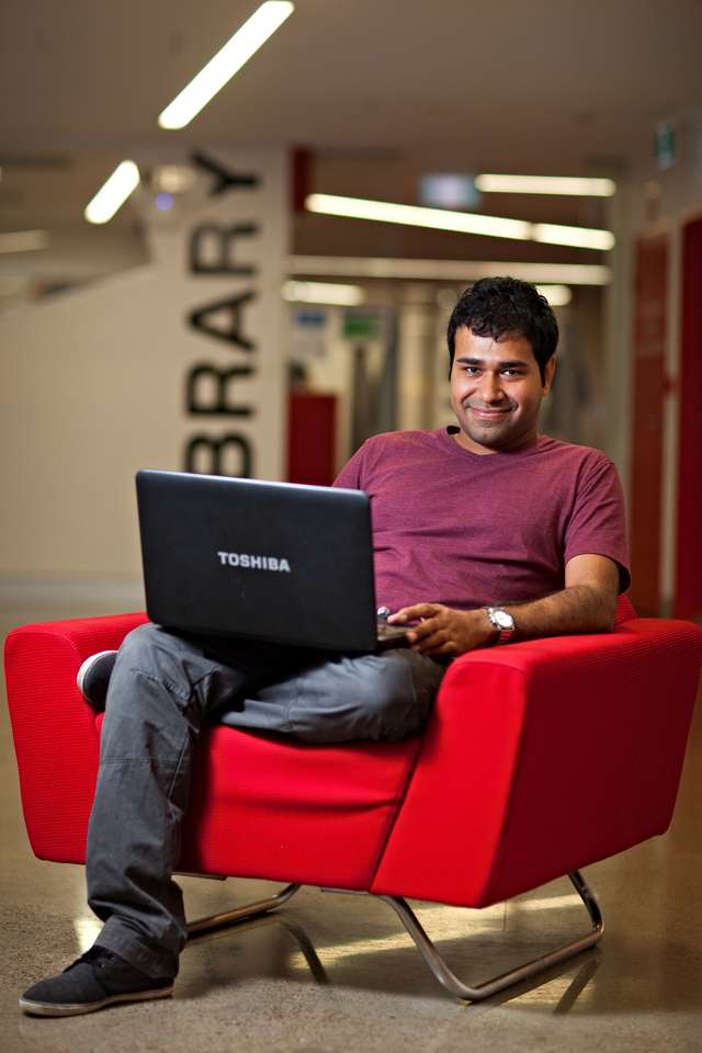 Student sits in a chair on campus while working on a laptop.