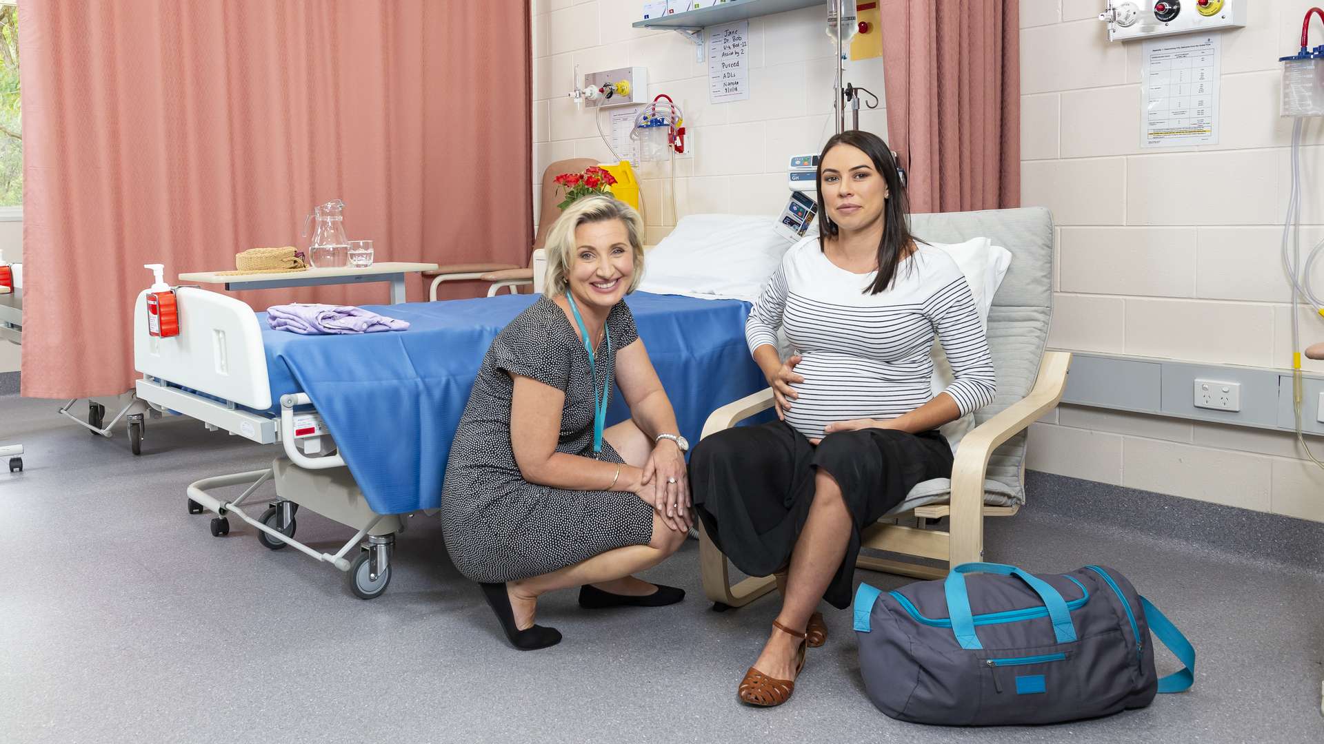 A CQU Midwifery student kneels next to a pregnant woman sitting in a chair in a hospital ward.